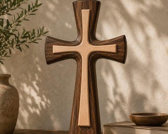 May include: A standing cross featuring a dark brown wood grain base with a lighter, smooth beige wood inlay centered in the middle. The cross has flared arms and a vertical orientation, showcasing a two-tone wood design with a polished finish.