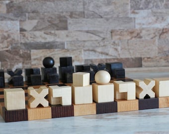 May include: A wooden chess set featuring a board with alternating light and dark brown squares. The pieces are geometric shapes, including cubes, spheres, and cross-like forms, rendered in contrasting light natural wood and solid black finishes.