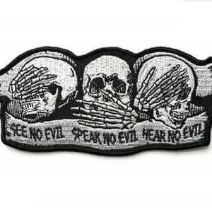 May include: Black and white embroidered patch with three skulls. The skulls are blindfolded, covering their ears, and covering their mouths. The text below the skulls reads "See No Evil Speak No Evil Hear No Evil".