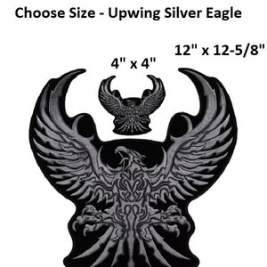 May include: A silver eagle with outstretched wings, embroidered on a black patch. The eagle is detailed with intricate designs and has a fierce expression. The patch is available in two sizes: 4 inches by 4 inches and 12 inches by 12 and 5/8 inches.