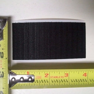 May include: A black hook and loop fastener, also known as Velcro, measuring 2 inches by 1 inch.