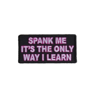 May include: Black embroidered patch with pink lettering that reads "SPANK ME IT'S THE ONLY WAY I LEARN".