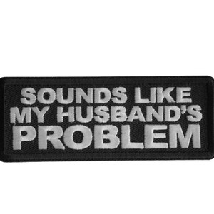 May include: Black rectangular patch with white embroidered text that reads "SOUNDS LIKE MY HUSBAND'S PROBLEM". The patch has a black border and is likely designed to be sewn or ironed onto clothing or accessories.