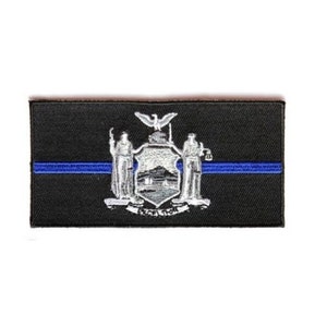 May include: Black embroidered patch with the New York State seal and a thin blue line across the center. The seal features a white eagle, two figures, and a shield with a mountain and a sun.