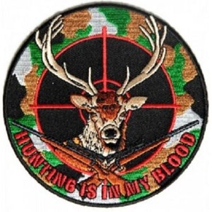 May include: A round, embroidered patch with a camouflage background. A deer's head is in the center of a red target with two rifles crossed behind it. The text "Hunting is in my blood" is written around the edge of the patch.