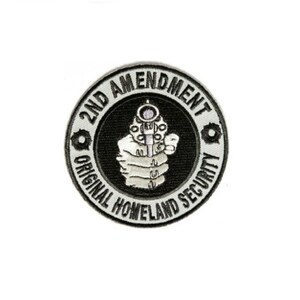 May include: A black and white embroidered patch with the text "2nd Amendment Original Homeland Security" in a circle around a hand holding a gun.