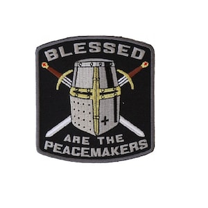 May include: A black and gray embroidered patch with a knight's helmet and crossed swords. The text reads "Blessed are the peacemakers".