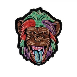 May include: Embroidered patch of a monkey's face with a colorful, psychedelic design. The monkey has a wide grin and its tongue is sticking out.