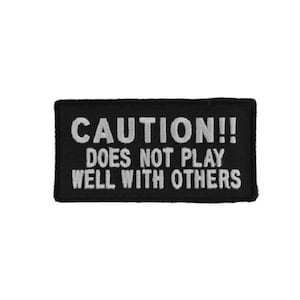 May include: Black and white embroidered patch with the text "CAUTION!! DOES NOT PLAY WELL WITH OTHERS".