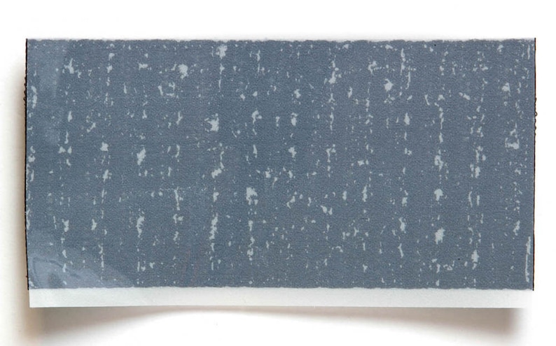May include: A close-up of a gray textured surface with a white background. The surface has a speckled pattern.