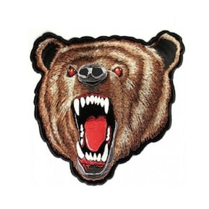 May include: A close-up of a brown bear's face with a fierce expression. The bear has red eyes and an open mouth with sharp teeth. The bear's fur is detailed with brown and black embroidery.