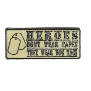 May include: A beige embroidered patch with the text "HEROES DON'T WEAR CAPES THEY WEAR DOG TAGS" and two dog tags.