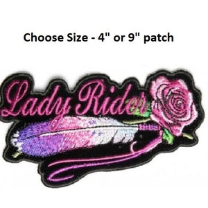 May include: Embroidered patch with the words "Lady Rider" in pink lettering, a pink rose, and a purple and pink feather. Choose Size - 4" or 9" patch.