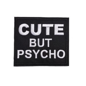 May include: Black square patch with white embroidered text that reads "CUTE BUT PSYCHO". The patch has a black border and is likely designed to be sewn or ironed onto clothing or accessories.