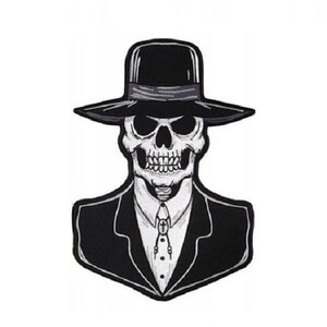 May include: Black and white embroidered patch of a skull wearing a black fedora and a suit. The skull has a serious expression and is wearing a tie with a cross pendant.