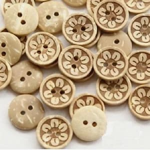 May include: A collection of round, natural coconut shell buttons with a floral design. The buttons are beige with a light brown floral pattern.