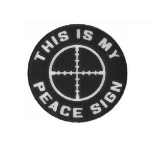 May include: A circular black embroidered patch featuring a white circular crosshair graphic in the center. The text THIS IS MY PEACE SIGN is stitched in white capital letters around the perimeter of the crosshair on the black background.