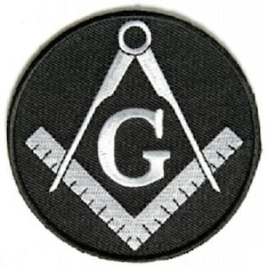 May include: A black circular patch featuring a white Masonic symbol. The symbol includes a compass, a square, and the letter "G" in the center. The patch is likely made of fabric and has a stitched border.