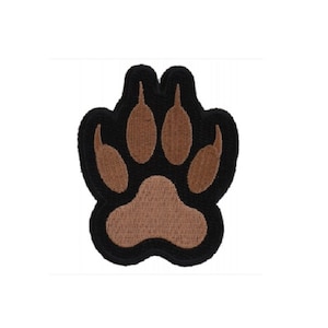May include: Brown paw print embroidered patch with black outline. The patch is made of felt and has a stitched design.