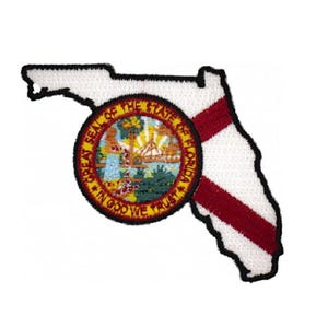 May include: An embroidered patch shaped like the state of Florida with a white background and a red diagonal stripe. Centered on the patch is a circular emblem featuring the Great Seal of the State of Florida with the text In God We Trust.