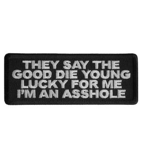 May include: Black rectangular patch with white embroidered text: "THEY SAY THE GOOD DIE YOUNG LUCKY FOR ME I'M AN ASSHOLE."