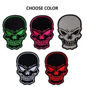 May include: Five embroidered skull patches in different colors. The skulls are black with white eyes and teeth. The patches are available in green, pink, gray, white, and red.