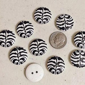 May include: A collection of ten round, wooden buttons with a black and white zebra stripe pattern. One button is plain white with two black dots.