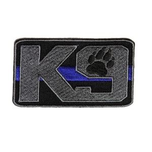 May include: A black and gray embroidered patch with the text "K9" and a paw print. The patch has a thin blue stripe across the middle.