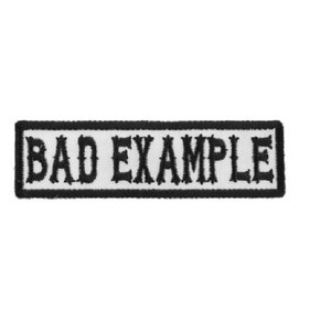 May include: Black and white embroidered patch with the text "BAD EXAMPLE" in a bold, stylized font.
