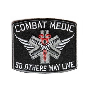 May include: Black embroidered patch with a red medical cross, two crossed knives, and wings. The text "Combat Medic" is above the cross and "So Others May Live" is below.