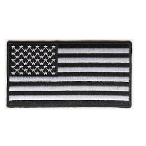 May include: A black and white embroidered American flag patch. The stars and stripes are white on a black background.