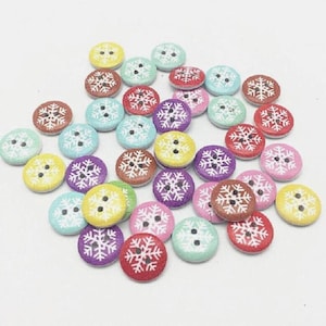 May include: A collection of round, flat buttons in various colors including red, yellow, pink, purple, and light blue. Each button features a white snowflake pattern printed on the surface and two small holes in the center for attachment.
