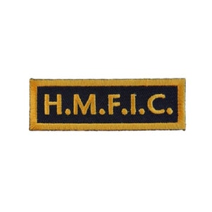 May include: A black embroidered patch with a gold border. The patch says "H.M.F.I.C."