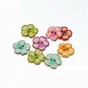 May include: Assortment of eight wooden flower-shaped buttons in various colors, including green, pink, blue, orange, and yellow. Each button has two holes and a floral design.
