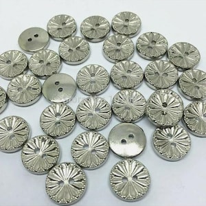 May include: A collection of silver-toned buttons with a decorative floral design. The buttons have two holes and are arranged in a random pattern.