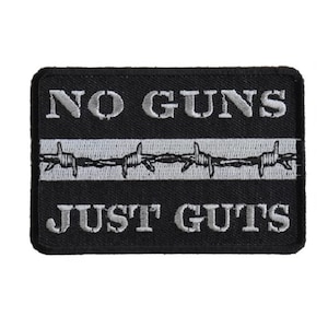 May include: Black and white embroidered patch with the text "NO GUNS JUST GUTS" and a barbed wire design.
