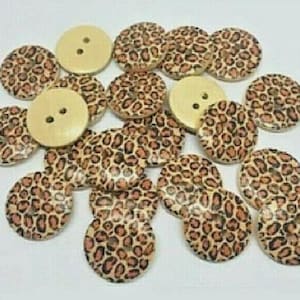 May include: A collection of wooden buttons with a leopard print design. The buttons are beige with brown spots and have two holes.