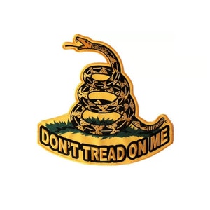 May include: A yellow patch featuring a coiled rattlesnake above green grass. The patch has the text "DON'T TREAD ON ME" in bold, black letters. The snake is gold and black.