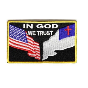 May include: A black embroidered patch with a yellow border. The patch features an American flag and a Christian flag overlapping. The text "In God We Trust" is embroidered in white on the patch.