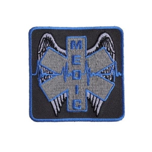 May include: Embroidered patch featuring the Star of Life symbol, with the word "MEDIC" in blue letters. The patch has a gray background with blue accents and a blue border. The design includes stylized wings and a heartbeat line.