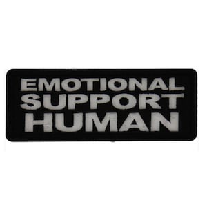May include: A black rectangular patch with the words "EMOTIONAL SUPPORT HUMAN" in white, block letters. The patch has a simple, clean design, suitable for attaching to clothing or bags.
