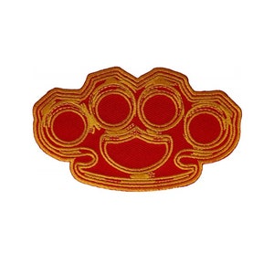 May include: Red and gold embroidered iron-on patch of a brass knuckle.