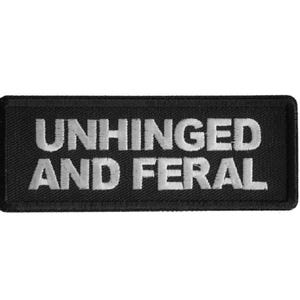 May include: Black rectangular patch with the words "UNHINGED AND FERAL" embroidered in white. The patch has a black border and is likely made of fabric.