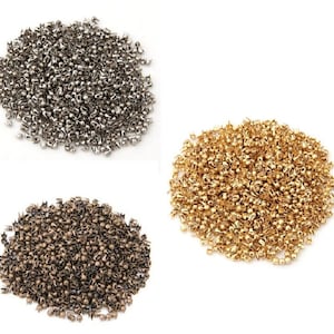 May include: Three piles of small metal rivets, one pile is silver, one is gold, and one is bronze.