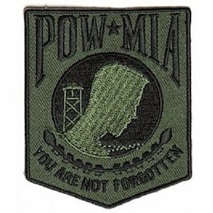 May include: A green embroidered patch with the words "POW*MIA" and "You Are Not Forgotten" in black. The patch features a silhouette of a prisoner of war camp with a watchtower.