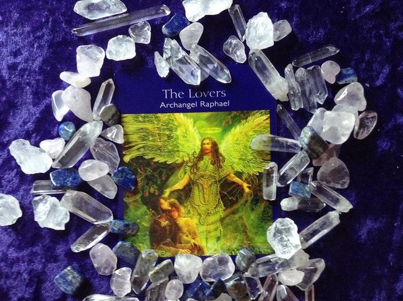 Peut inclure: Une carte de tarot avec un fond bleu et les mots "The Lovers, Archangel Raphael" imprim&eacute;s dessus. La carte pr&eacute;sente une illustration d'un ange avec des ailes dor&eacute;es et une aur&eacute;ole, debout dans un d&eacute;cor de for&ecirc;t. L'ange porte une robe verte et dor&eacute;e et tend les mains vers un couple assis au sol. La carte est entour&eacute;e de cristaux de quartz clair et de cristaux de lapis-lazuli bleus.