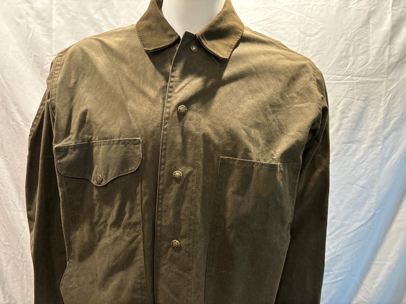 Puede incluir: Una camisa verde de manga larga con botones, dos bolsillos de solapa y cuello de pana.