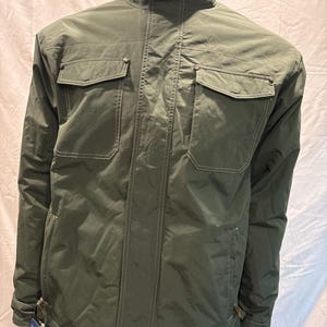 May include: A dark green, lightweight jacket with a zipper closure and two large flap pockets. The jacket has a stand-up collar and a drawstring at the waist.