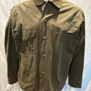 Puede incluir: Una camisa de manga larga de color verde oliva con cuello de ante y varios bolsillos. La camisa tiene cierre de botones en la parte delantera y botones de lat&oacute;n.