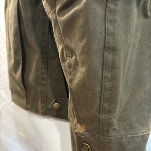 Puede incluir: Una chaqueta de lona verde con un parche de cuero marr&oacute;n en la manga. La chaqueta tiene cierre de botones y un bolsillo con bot&oacute;n en el lado izquierdo. La chaqueta tiene una etiqueta que dice "Field Co. Sports" en la parte inferior de la manga.